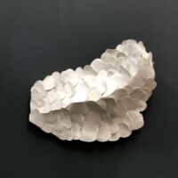 New Moon features white, overlapping ceramic shapes arranged in an abstract, wing-like formation and mounted on a dark wall.