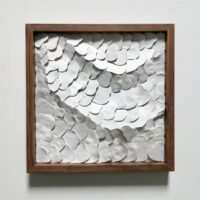 A wooden-framed artwork featuring overlapping white, petal-like ceramic pieces arranged in an abstract, textured pattern against a plain background.