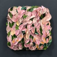 A square wall sculpture featuring layered ceramic leaves in shades of pink, green, and yellow against a dark background.